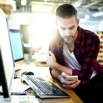 man sitting in front of a laptop checking his phone